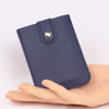 A dark blue slim PU leather card wallet with a stitched flap and a silver stud closure is held in a hand.