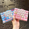 A hand holds a pink and blue cartoon animal stress relief keychain with a keyboard design.