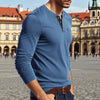 A man wearing a blue long-sleeve shirt with a collar and chest pocket standing in a European square.