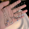 A hand holds a display of silver and iridescent crystal bow angel wings heart pendant necklaces.