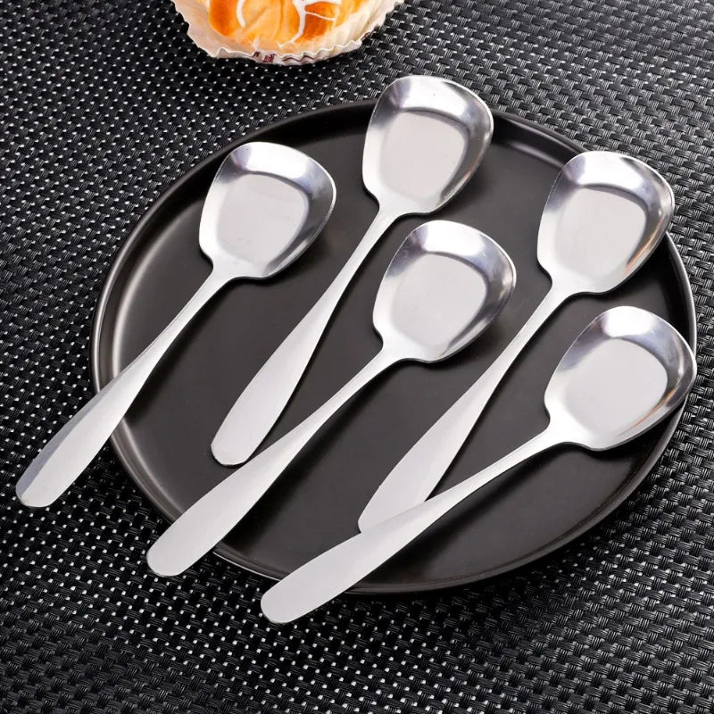 A set of five stainless steel serving spoons arranged on a dark plate.