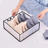 A hand is placing folded underwear and socks into a black organizer with dividers.
