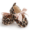 Pair of leopard print baby first walkers with soft pink ribbon accents and natural rubber soles.