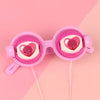 A pair of pink novelty glasses with heart-shaped lenses and a string attached.