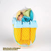 A clear mesh bag filled with a beach castle sand play set featuring blue and yellow plastic scoops and sand.
