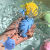 A hand is holding a blue squeezy whale bath toy submerged in water, with other toys visible.