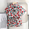 A red and green floral print shirt and shorts set for kids displayed on a hanger.