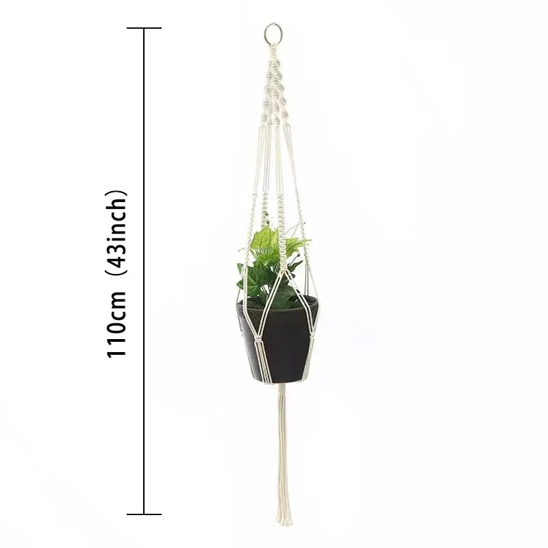 Macramé-plantekurv med hvit snor og grønn plante i svart potte, hengt opp i en løkke.