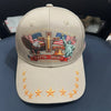 A beige baseball cap featuring a patriotic graphic design with an eagle, a cross, and a statue of liberty.
