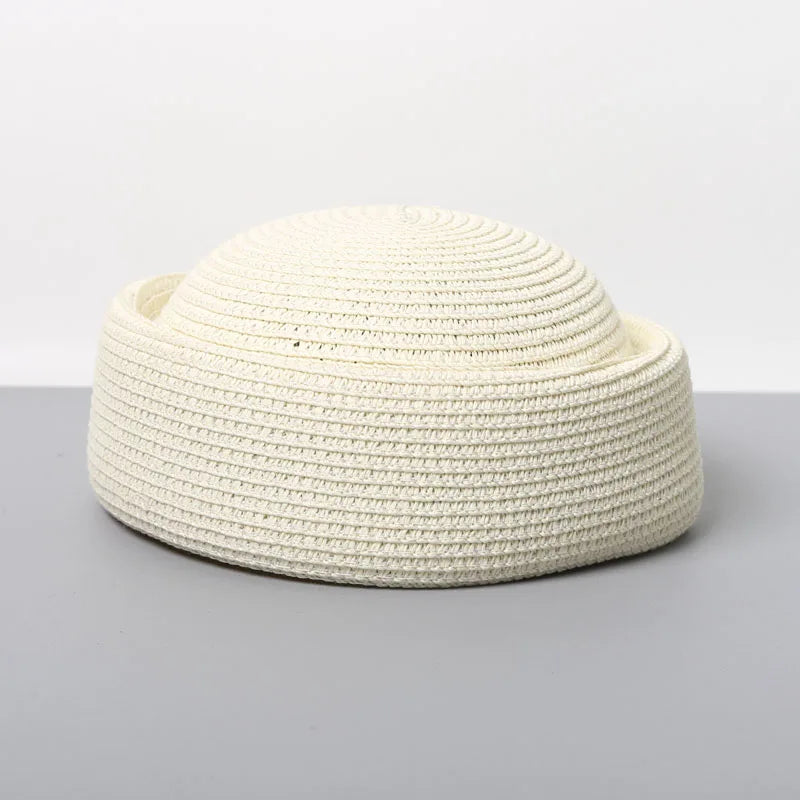 A beige straw pillbox sun hat with a wide brim shown against a gray background.