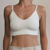A model wearing a white seamless U-back bralette top and light colored pants.