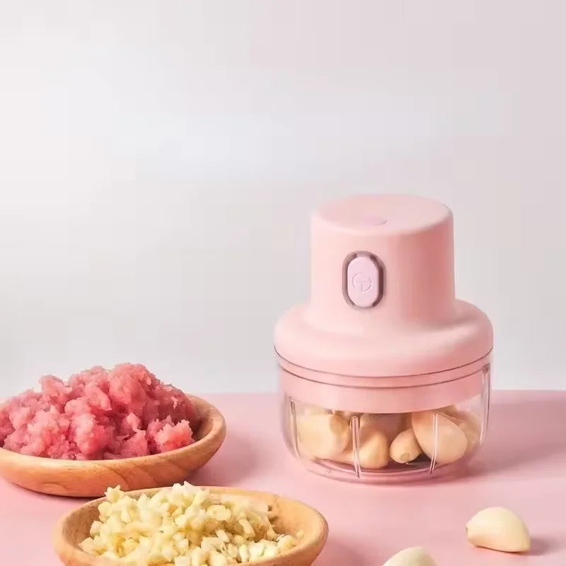 Rosa bærbar elektrisk foodprosessor med klar beholder fylt med hvitløk og ingefærbiter.