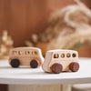 A light wooden hand-pushed cart toy for toddlers resting on a white surface with blurred natural elements in the background.