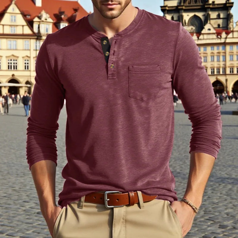 A man wearing a maroon long-sleeve casual shirt with a chest pocket and tan pants outdoors.