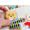 A hand holds a wooden puzzle of a bear dressed in a striped shirt, used for Montessori dress-up play.