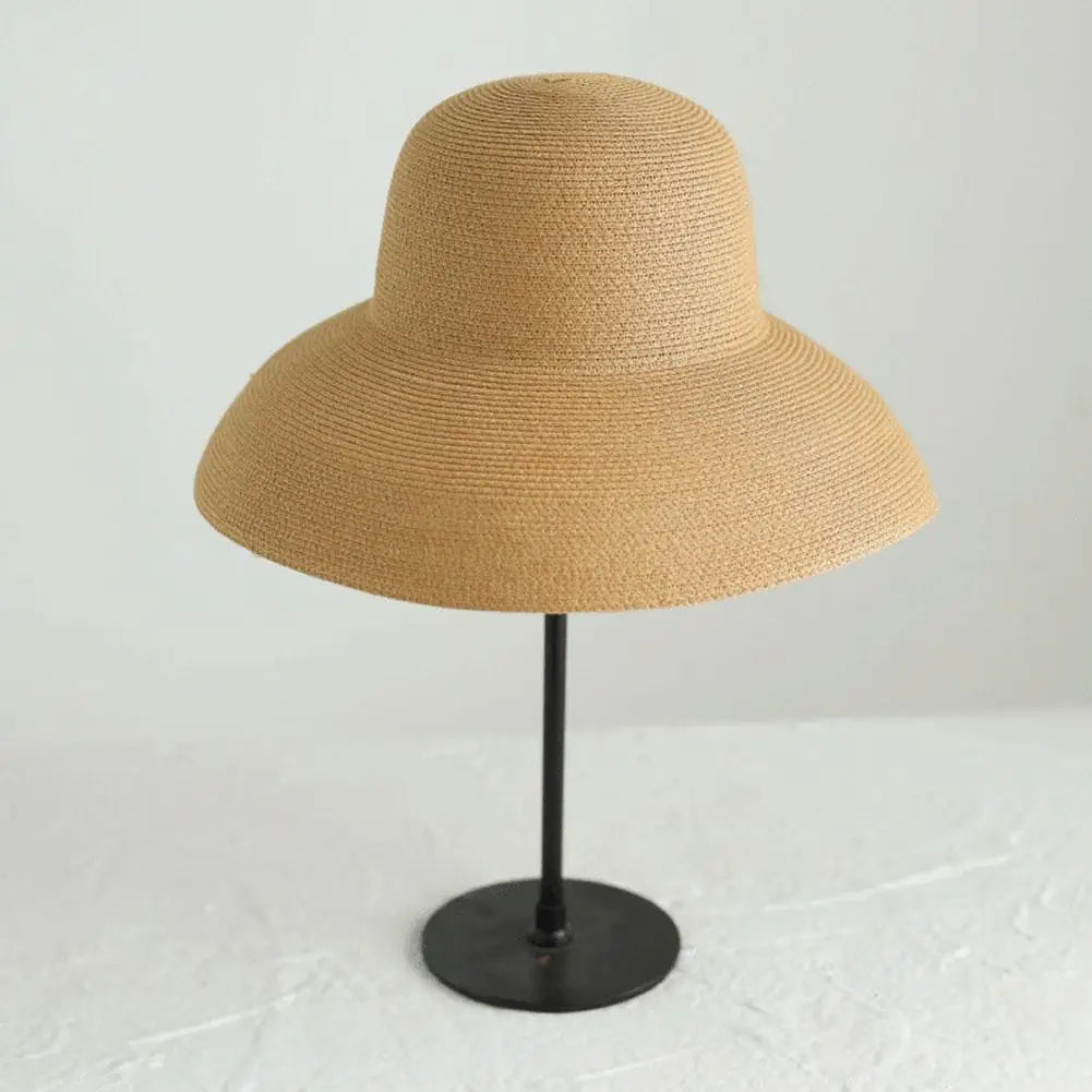 A wide brim straw sun hat in a natural beige color displayed on a black stand.
