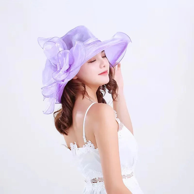 A woman wearing a purple organza sun hat with ruffled mesh and a white dress.