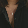 A close-up of a sterling silver water droplet pendant necklace with a zircon stone worn on a person's chest.