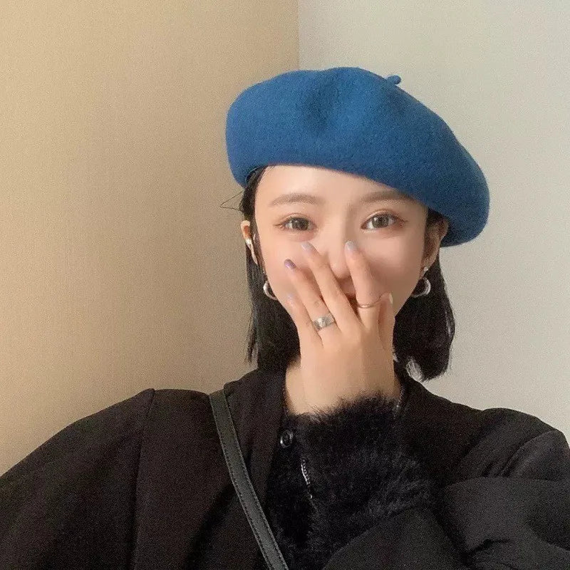 A woman wearing a blue wool beret hat and a black coat with a dark fur collar.