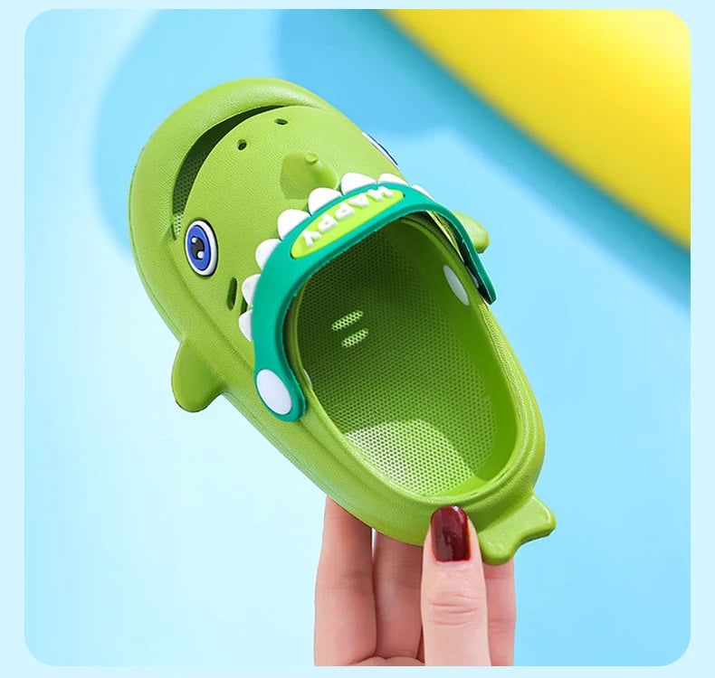 A hand holds a bright green kids shark clog sandal with a blue eye and a green strap.