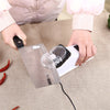 Hands are using an electric knife sharpener with a protective cover to sharpen chili peppers on a fabric surface.