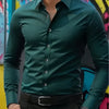 A man wearing a dark green long-sleeve formal shirt and black pants, posing in front of colorful graffiti.