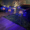 Colorful LED fireworks shooting from poles in a garden setting at night