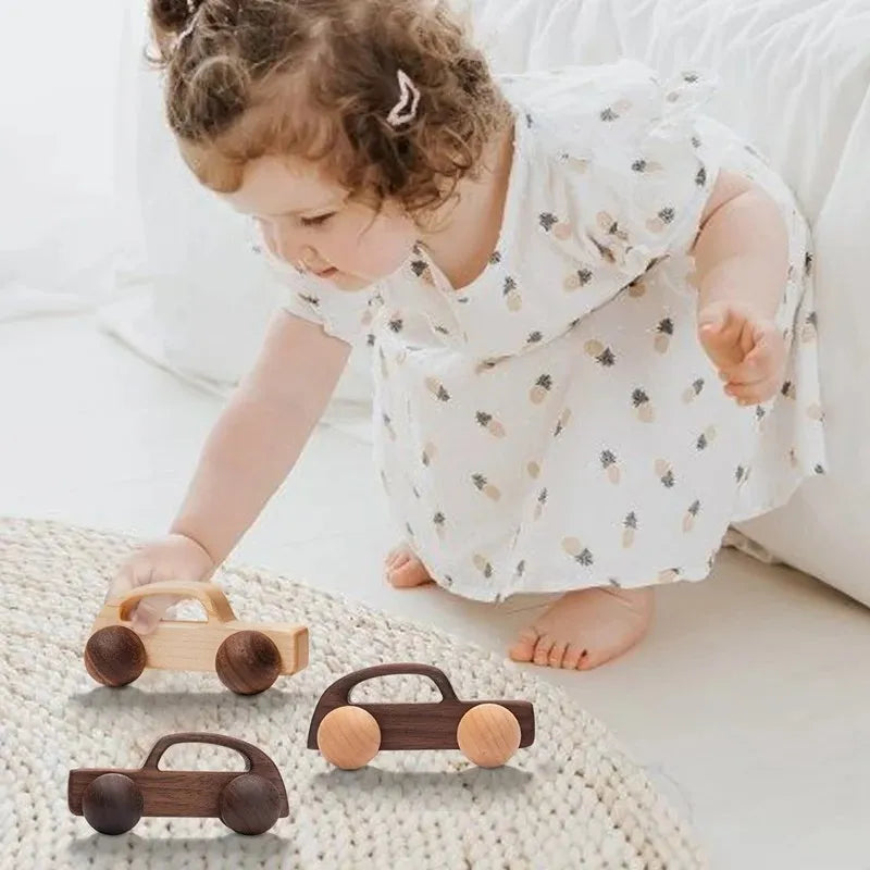 A young girl is playing with several hand-pushed wooden cart toys on a light-colored surface.