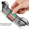 A hand holds a set of nine stainless steel measuring spoons with a magnetic design for convenient storage.