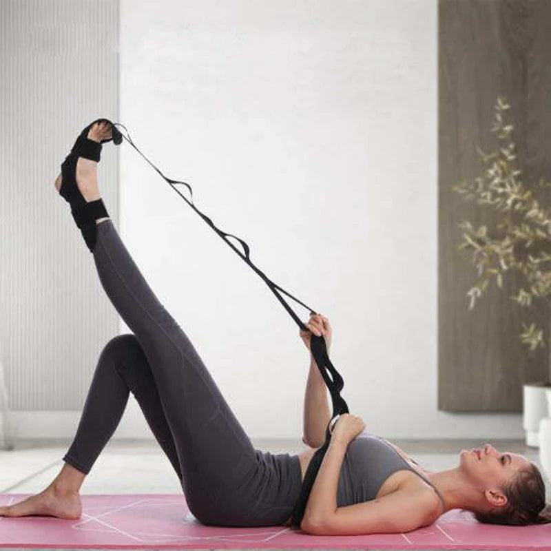 Mujer haciendo estiramiento de yoga con correa multibucle y cojines para pies sobre una colchoneta rosa.