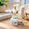 A white bird-shaped fidget keychain with a yellow base and blue light, resting on a wooden surface.