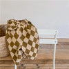 A pair of olive green checkered cotton harem pants with pockets displayed on a white wooden chair.