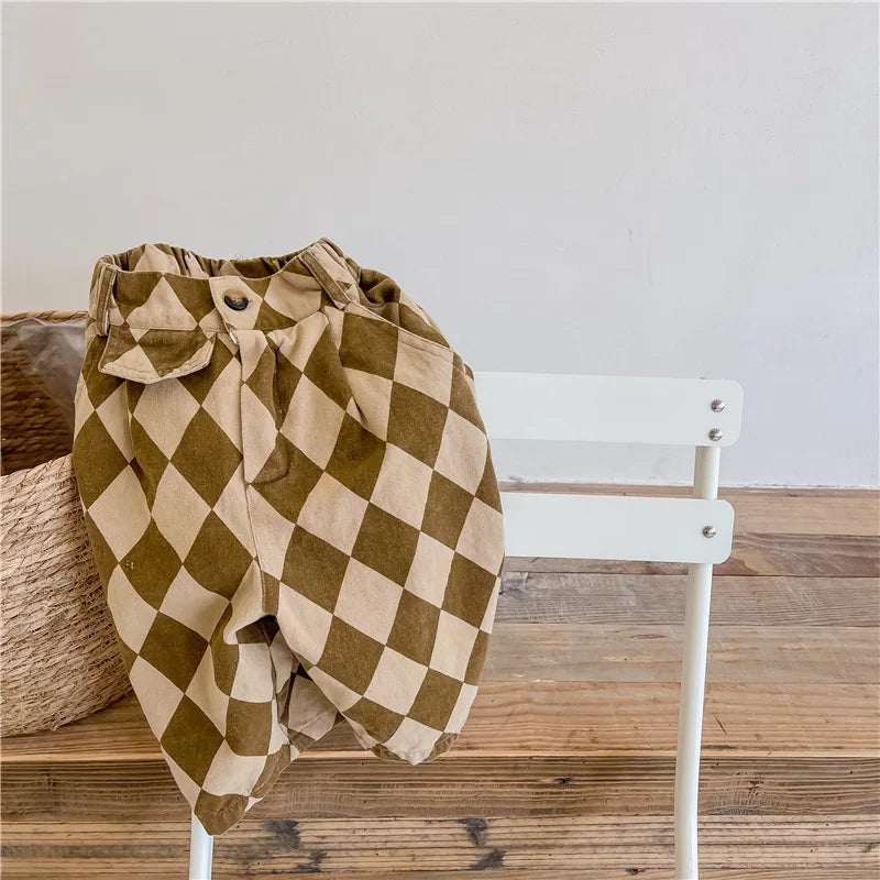 A pair of olive green checkered cotton harem pants with pockets displayed on a white wooden chair.
