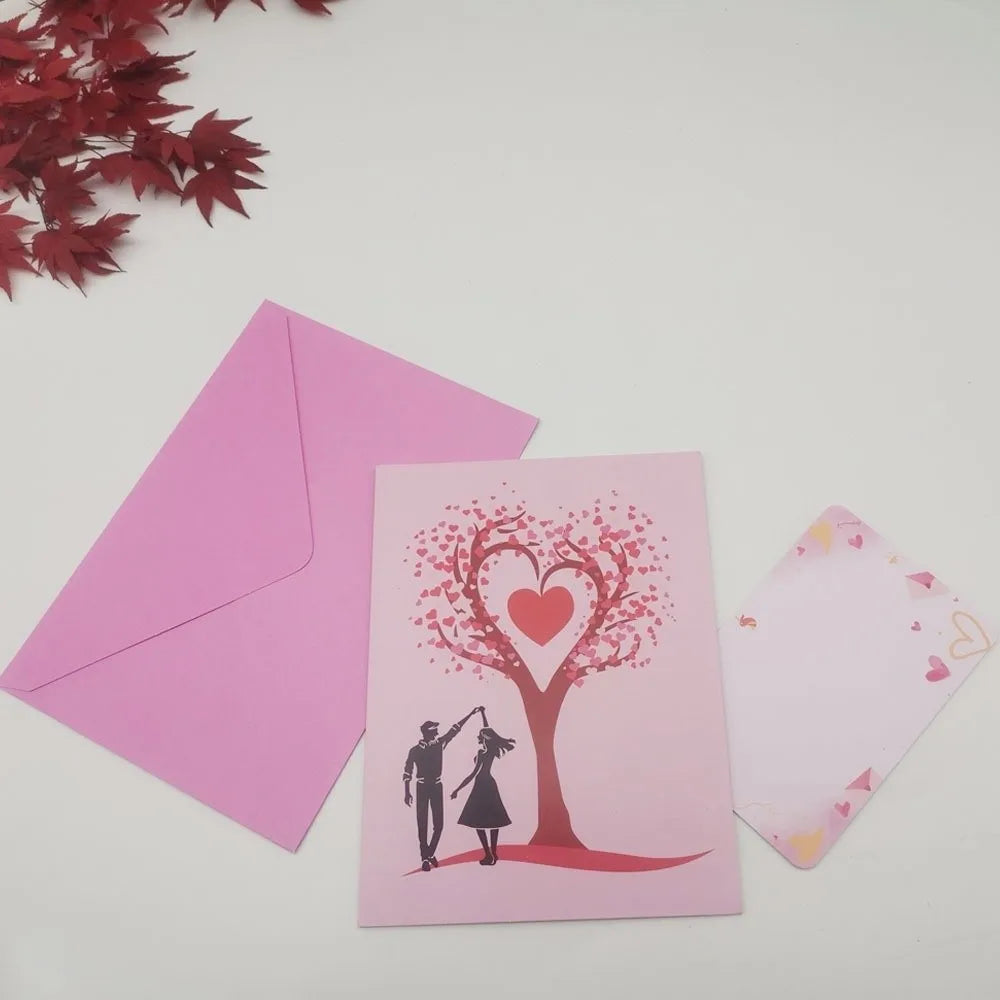 A pink pop-up card featuring a heart-shaped tree silhouette with a couple standing beneath it.