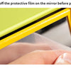 A hand is tearing off a protective film on the mirror of a yellow wooden spinning drum for toddlers.