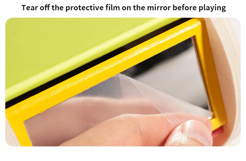A hand is tearing off a protective film on the mirror of a yellow wooden spinning drum for toddlers.