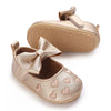 A pair of gold satin baby first walker shoes with a bow and heart patterns.