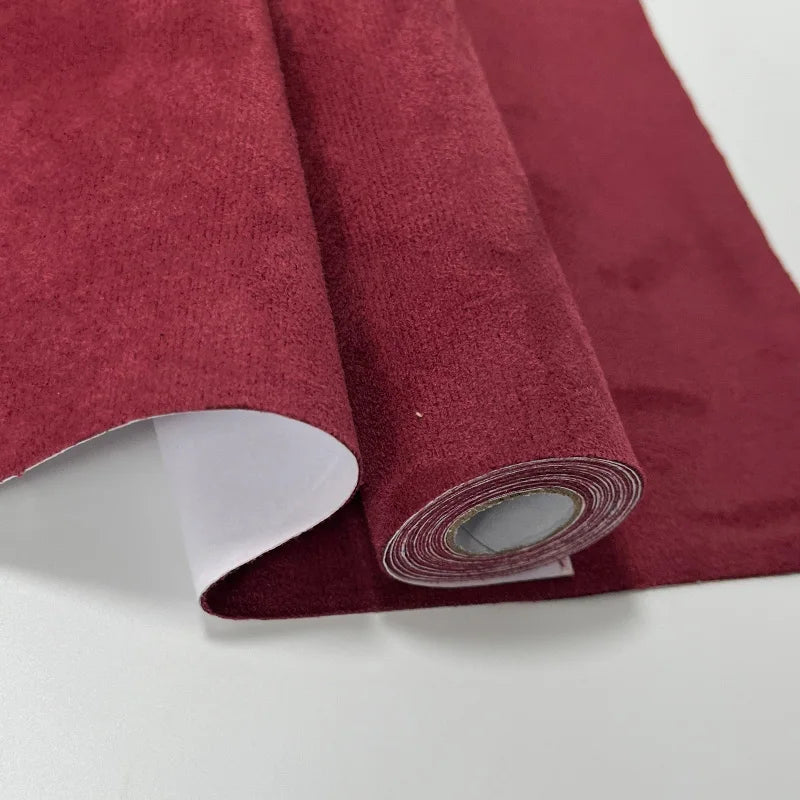 Rollo de tela de terciopelo ante granate oscuro con respaldo blanco visible.