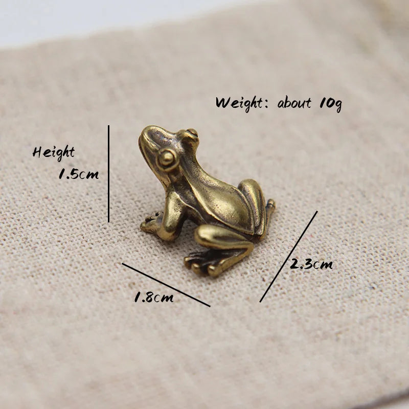 Liten vintage figurin av messingfrosk, 1,5 cm høy og 2,3 cm lang, på lys stoffoverflate.