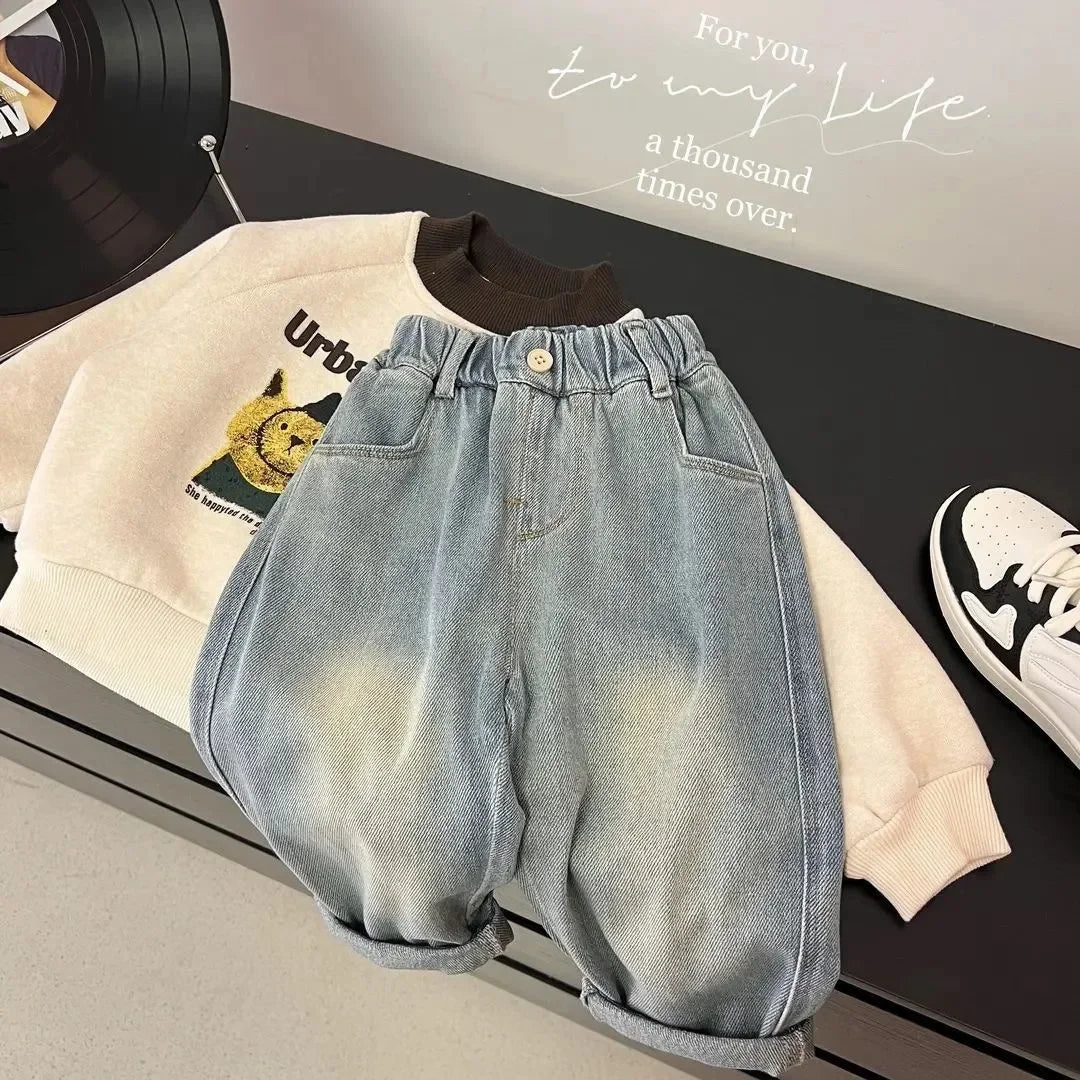 Light wash denim jeans and a cream sweatshirt laid out on a dark surface.