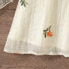 A light cream floral embroidered sleeveless dress for a baby girl lying on a wooden surface.