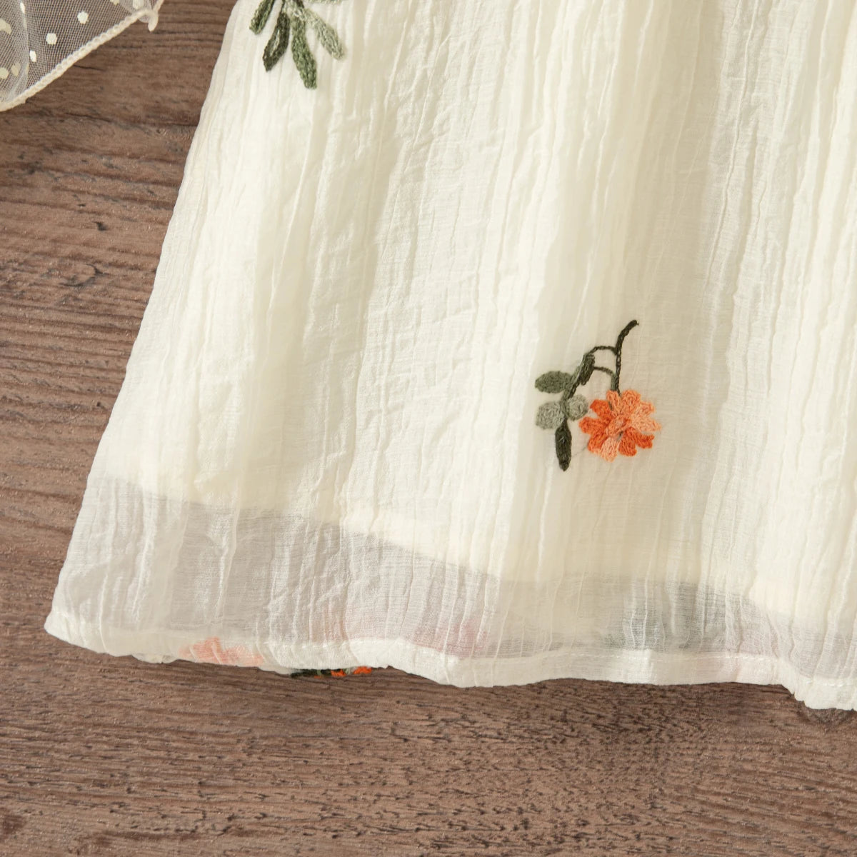 A light cream floral embroidered sleeveless dress for a baby girl lying on a wooden surface.