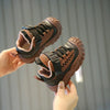 A hand holds a pair of brown and black breathable running sneakers for children against a gray background.