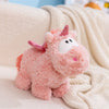 A pink unicorn plush toy with a sparkly horn is resting on a cream-colored knitted blanket.