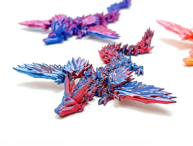 Primer plano de una figura de escritorio de dragón articulado impreso en 3D en tonos azules y rosados.
