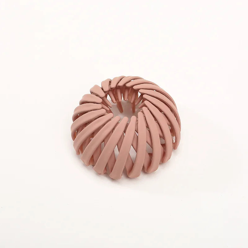 مشبك شعر على شكل عش طائر هندسي بلون وردي غبار أو بيج.