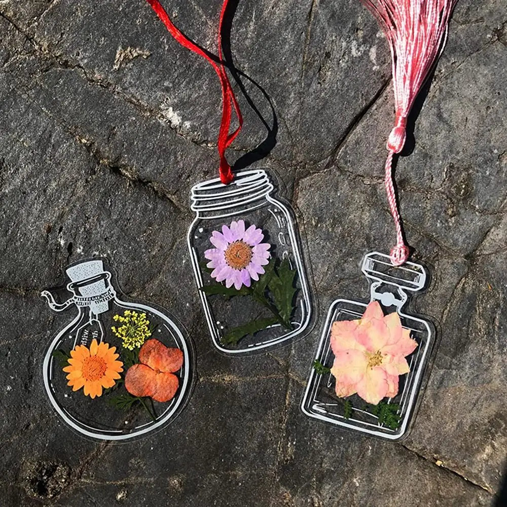 Three glass jars containing dried flowers and attached with red and pink twine for bookmarks