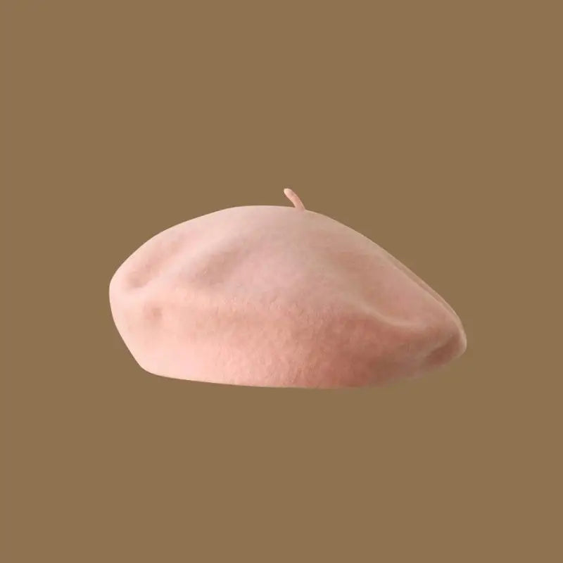 A soft pink classic wool beret hat for women shown against a brown background.
