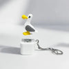 A white and gray seagull-shaped keychain fidget toy with a yellow beak, resting on a white plastic base.