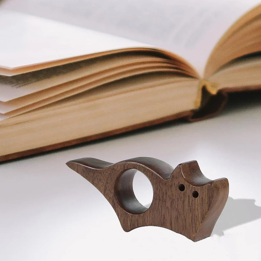 Juego de marcapáginas de madera de gato y perro sobre una superficie blanca junto a un libro abierto.